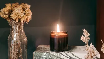 Kerze brennt neben getrockneten Blumen in der Vase.