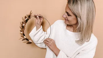 Person holding dried floral wreath indoors.