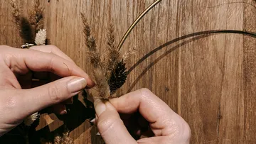 Hands arranging dried flowers on wood.