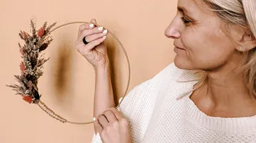 Woman holding decorative hoop with dried flowers indoors.