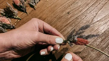 Hands crafting a floral wreath on wood table.