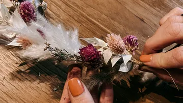 Hands creating dried flower wreath on table.