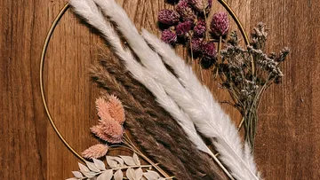 Getrocknete Blumen und Gräser, angeordnet auf einer Holzoberfläche.
