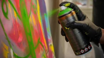 Gloved hand spray-painting colorful graffiti.