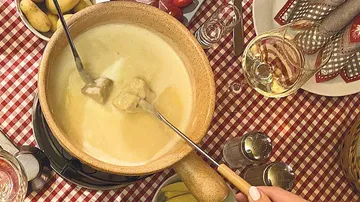 Cheese fondue pot with forks on checkered tablecloth.