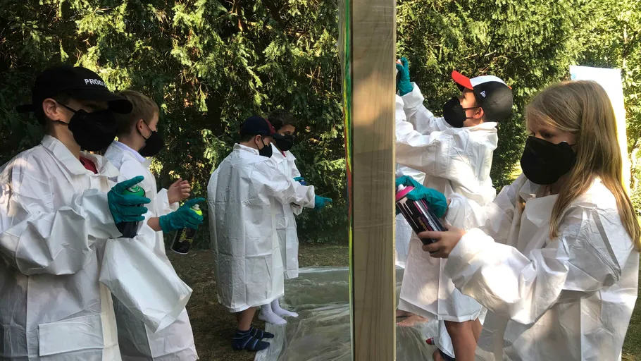 Children spray painting in protective gear outdoors.