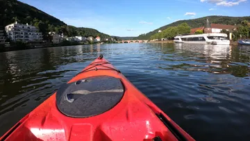 Rotes Kajak auf einem Fluss mit entfernter Brücke.