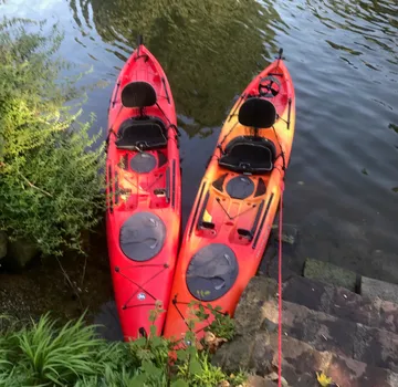 Two red-orange kayaks docked on a riverbank.