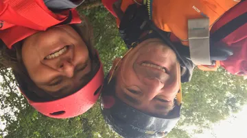 Zwei Menschen, die Helme tragen und draußen lächeln.