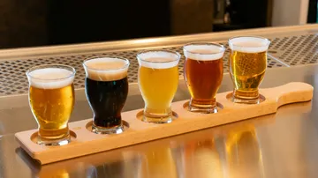 Five beer glasses on wooden flight board.