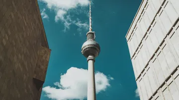Television tower between two buildings, cloudy sky.