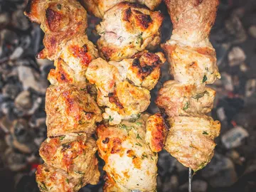 Gegrillte Fleischspieße brutzeln über glühenden Kohlen im Freien.