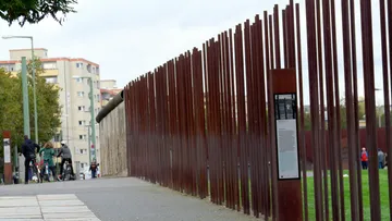Gedenkzaun mit Hinweisschild, städtisches Umfeld.