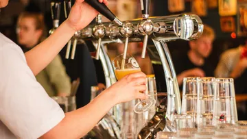 Person pours draft beer in bar setting.
