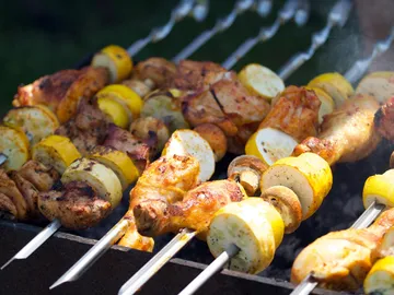 Grillspieße mit Fleisch und Gemüse in einer grünen Umgebung.