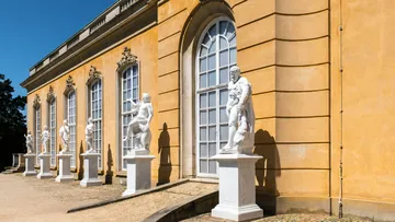 White statues in front of an orange building.