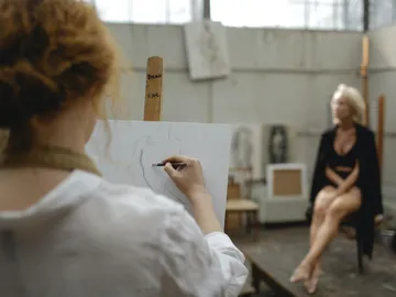 A person draws a naked figure in a studio.
