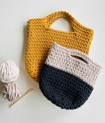 Zwei Häkelbeutel, eine gelbe, eine schwarze und eine beige.