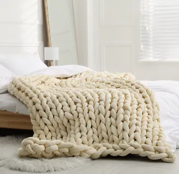 Grob gestrickte Decke auf einem Bett in einem hellen Raum.