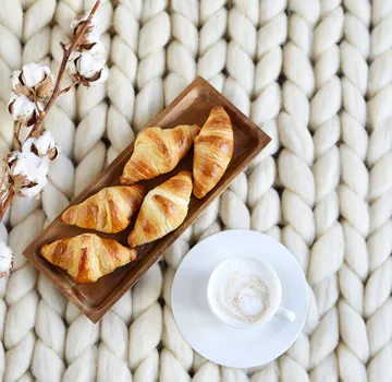 Croissants auf einer Platte, Baumwollzweig, Kaffee auf gestrickter Oberfläche.