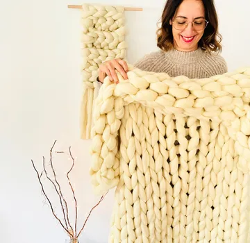 Frau hält eine grob gestrickte Decke drinnen in der Hand.