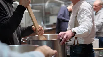 People stirring large pots in a kitchen.