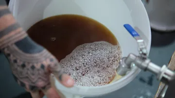 Person pouring liquid from tap into a bucket.