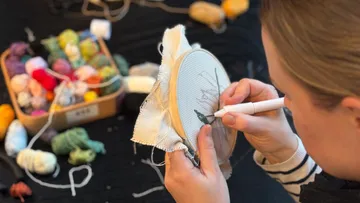 Person embroidering with yarn colors nearby.