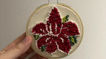 Hand-embroidered red flower in wooden hoop.