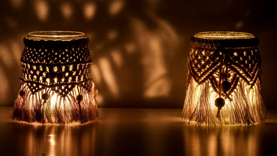 Two glowing lanterns with macrame covers on a table.