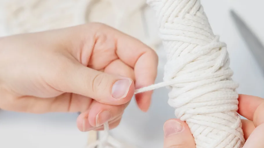 Hands wrapping white rope around stick.