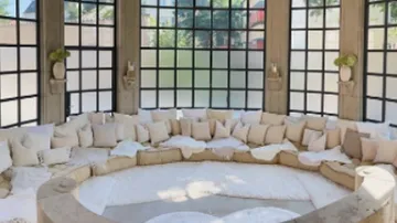 Rundes Sofa mit Kissen, große Fensterumrandung.