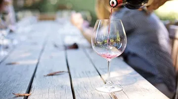 Wein wird in ein Glas auf einem Holztisch gegossen.