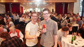 Zwei Personen mit Mikrofon bei überfüllter Veranstaltung.