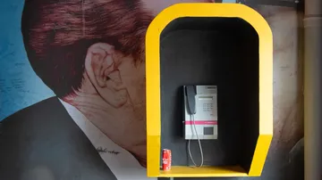 Payphone in yellow booth with Coca-Cola can.