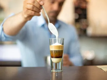 Eine Person gießt Milch in ein Glas mit Kaffee.