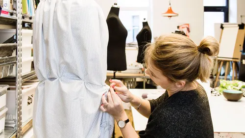 Designer heftet Stoff auf eine Schaufensterpuppe im Studio.