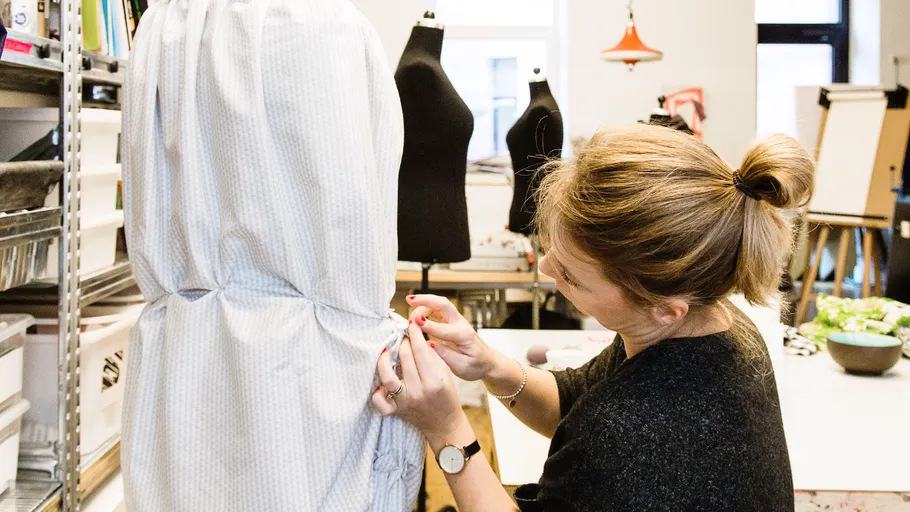 Designer heftet Stoff auf eine Schaufensterpuppe im Studio.