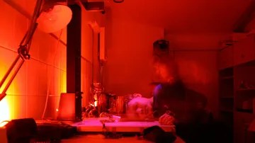 Person in red-lit darkroom with photo equipment.
