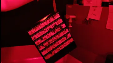 Photographic film strip in red-lit darkroom.