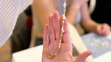 Hand haltend eine Halskette mit Perlen und Kette.