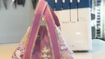 Violette Stofftasche vor der Nähmaschine.
