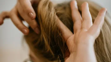 Hände, die Haare zu einem Knoten zusammenfügen.