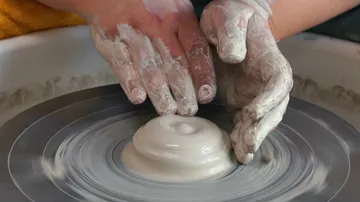 Hands shaping clay on a pottery wheel.
