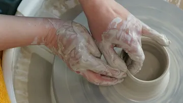 Hands shaping clay on a pottery wheel.