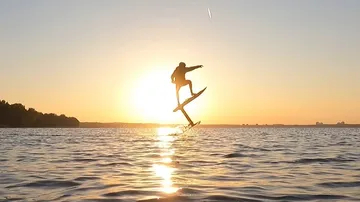 Person foil surfing at sunset on water.