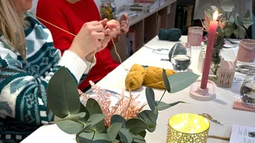 Two people knitting at a table with candles.