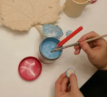 Person painting small clay disc with blue paint.
