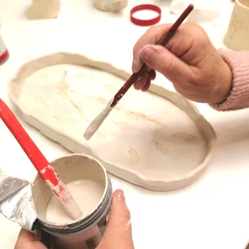 Hands painting ceramic tray with brush and glaze.