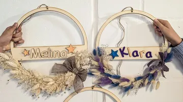 Hände halten Namenskränze aus Holz mit getrockneten Blumen.
